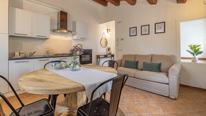 A modern kitchen with white cabinets, a wooden dining table, and a beige sofa in a living area. - La Finestra sul Mare - Apartment with a view (Gabicce Mare)