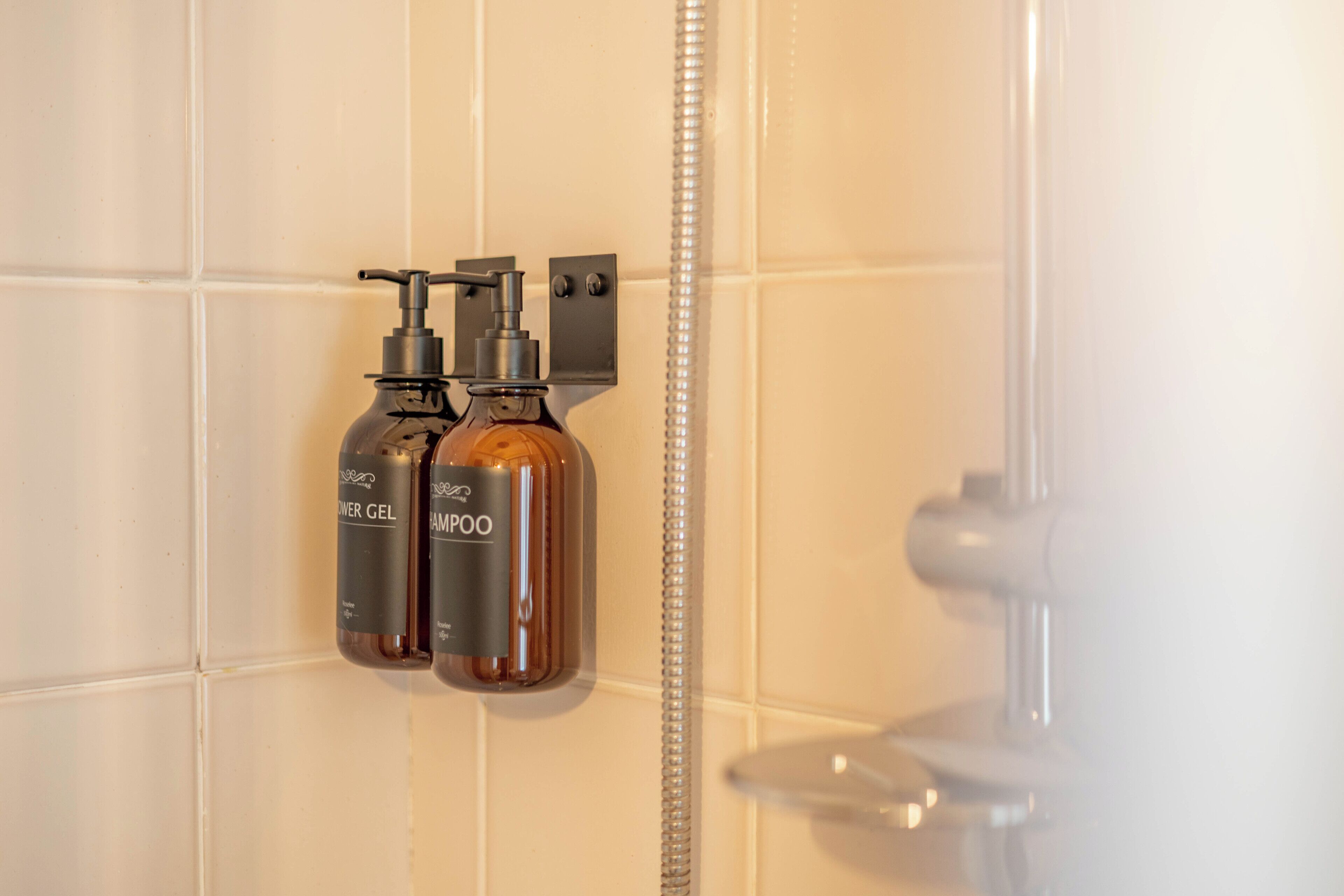 A bathroom with two bottles of shower gel and shampoo mounted on the wall.