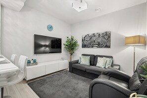 Una sala de estar moderna con un televisor de pantalla plana, un sofá, un comedor y una planta.