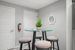 A room with a glass table, four stools, a potted plant, a white door, and a white-framed mirror. - Calgary Modern Suite • AC • Free Driveway Parking (Calgary)