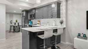Une cuisine moderne avec des meubles gris, un îlot central doté de tabourets, un four à micro-ondes et un évier.