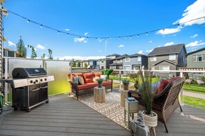 Una terraza con una parrilla, mobiliario exterior y vistas a casas vecinas.