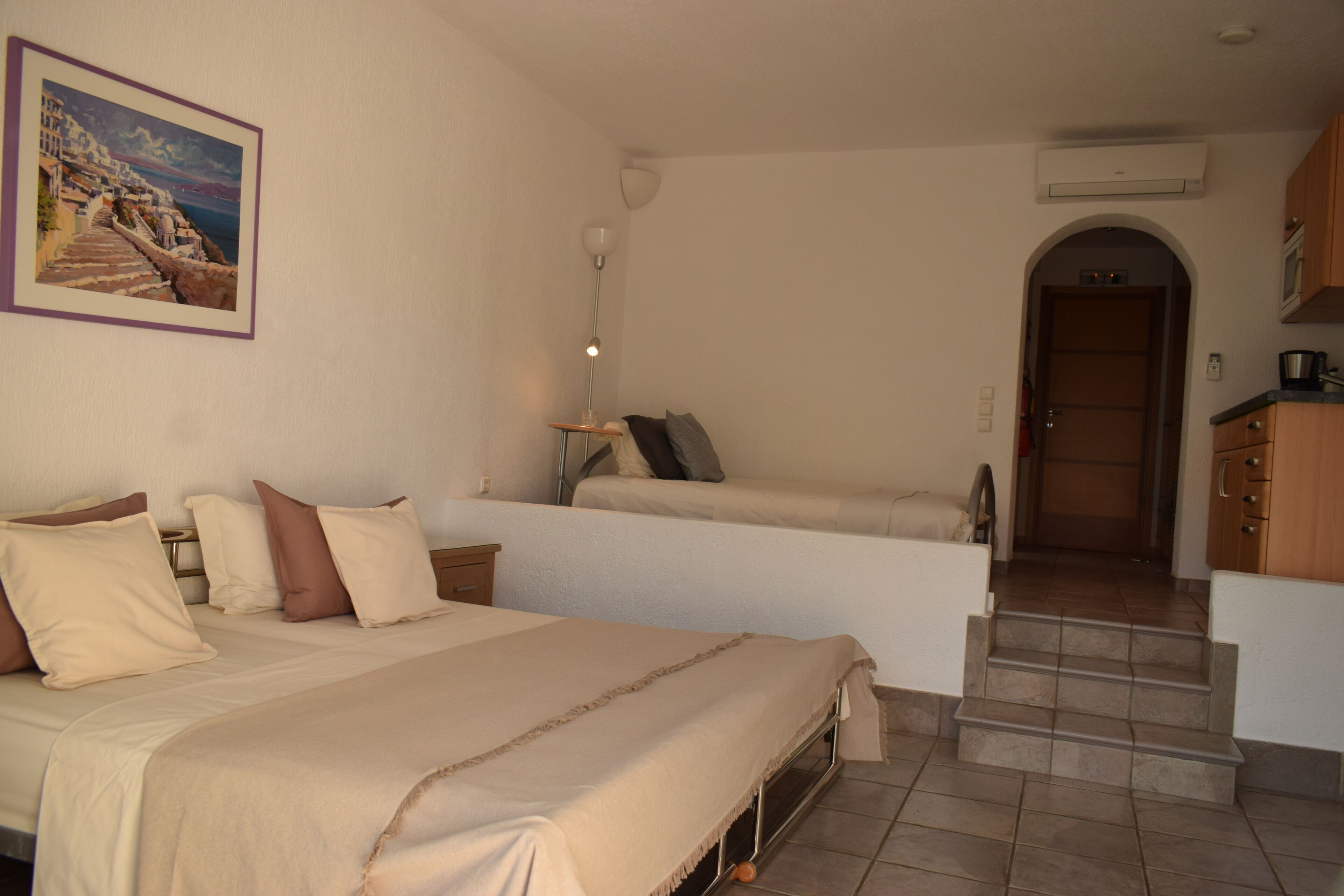 Een slaapkamer met een bed, nachtkastjes, een lamp, een schilderij en een uitzicht op een trap die naar een deur leidt.