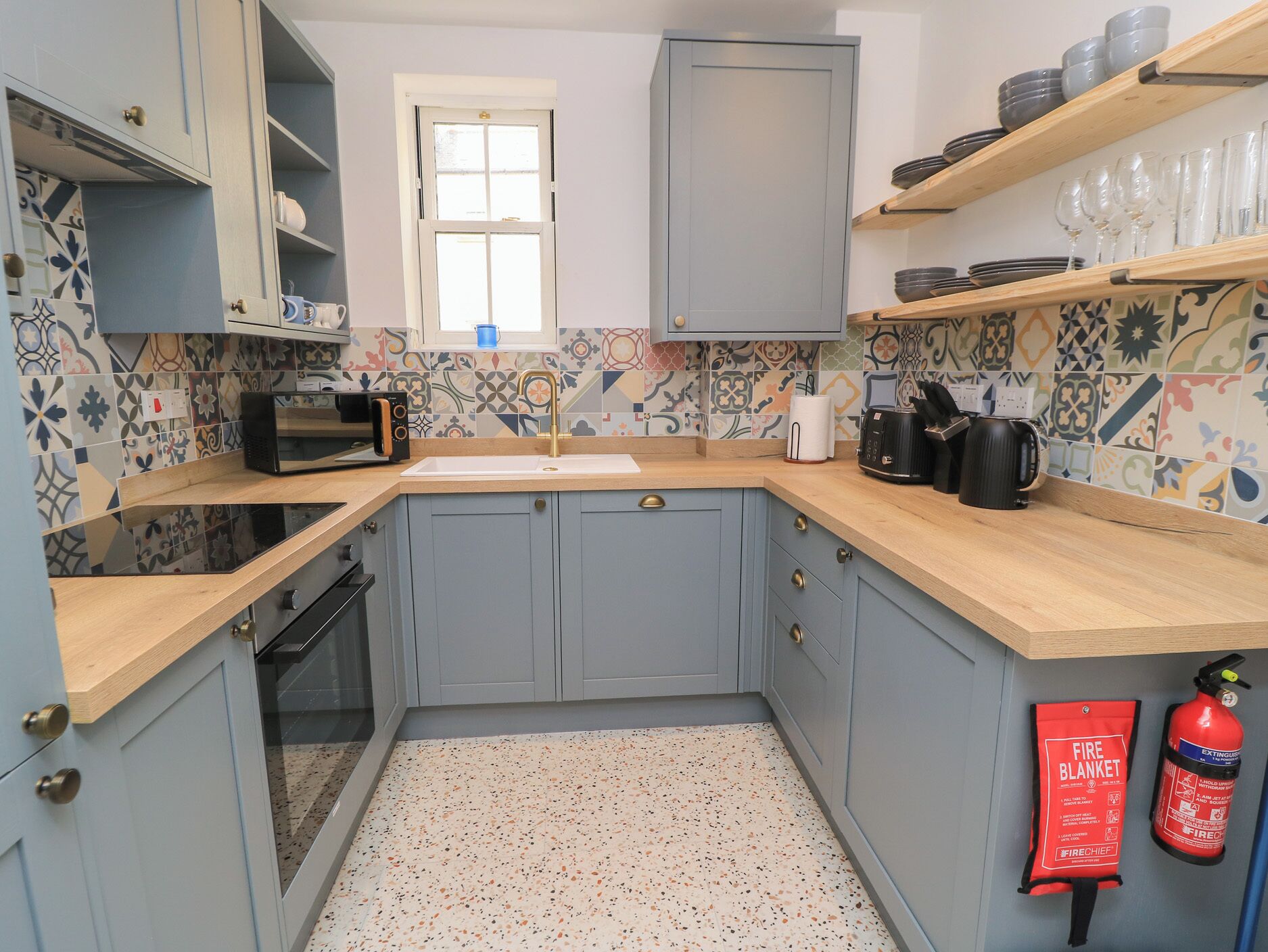 A kitchen with blue cabinets, a microwave, a sink, and a fire extinguisher.