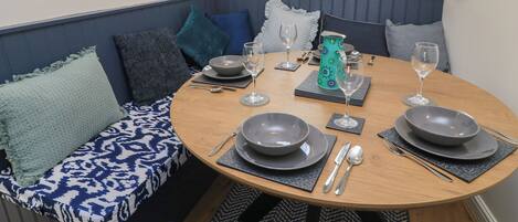 Uma sala de jantar com uma mesa redonda posta para quatro pessoas, rodeada por um banco acolchoado azul.