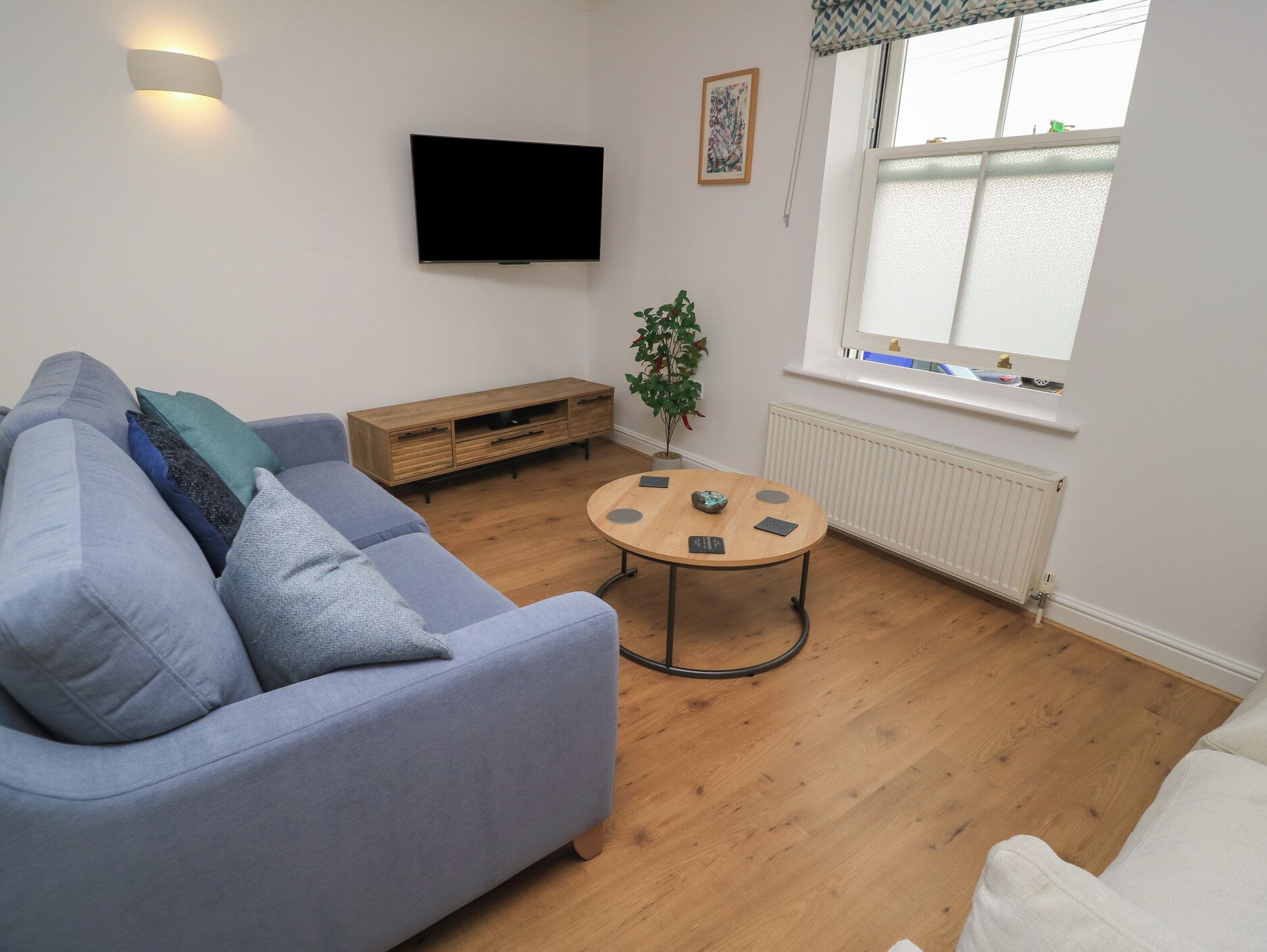 Ein Wohnzimmer mit Sofa, Couchtisch, Fernseher, Fenster und Heizkörper.