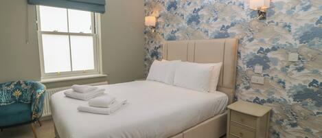 A bedroom with a bed, a nightstand, a chair, and a window with a blue curtain.