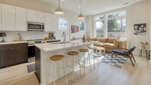 A modern kitchen with a central island, bar stools, and a dining area with a sofa and coffee table. - 2 New Townhomes w/ Balcony, Mins to Broadway, Sleeps 16 | 98 Degrees & The Stage (Nashville)