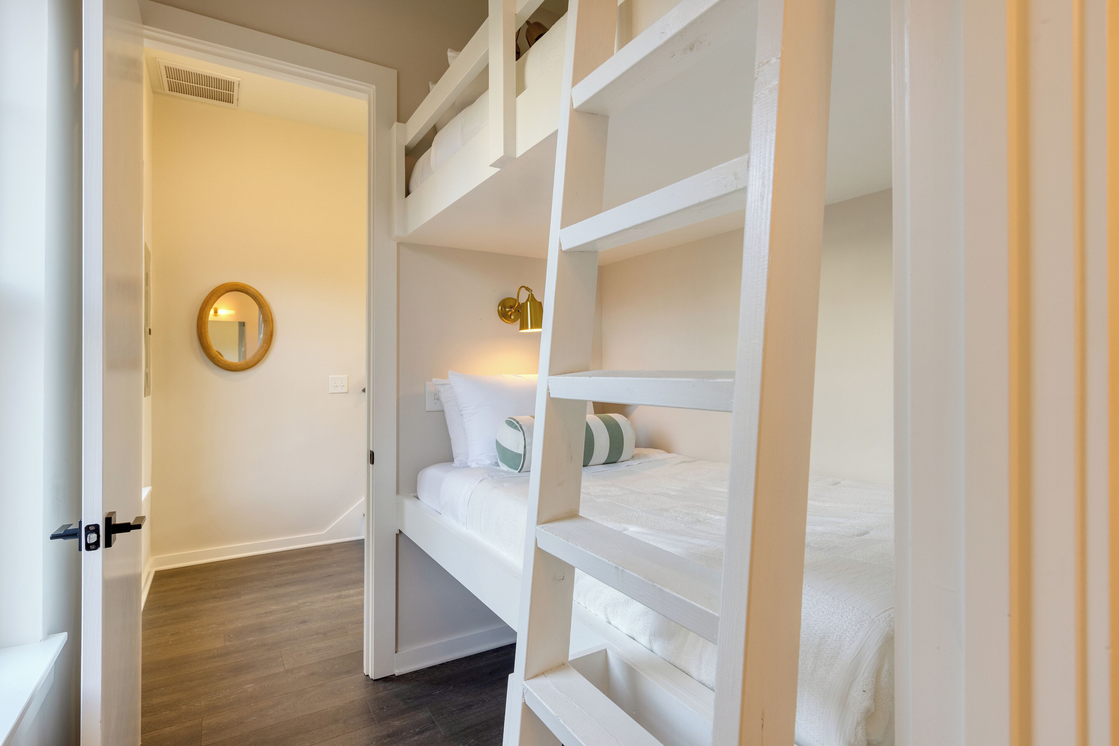 Una habitación con literas, un espejo redondo y una lámpara de pared.