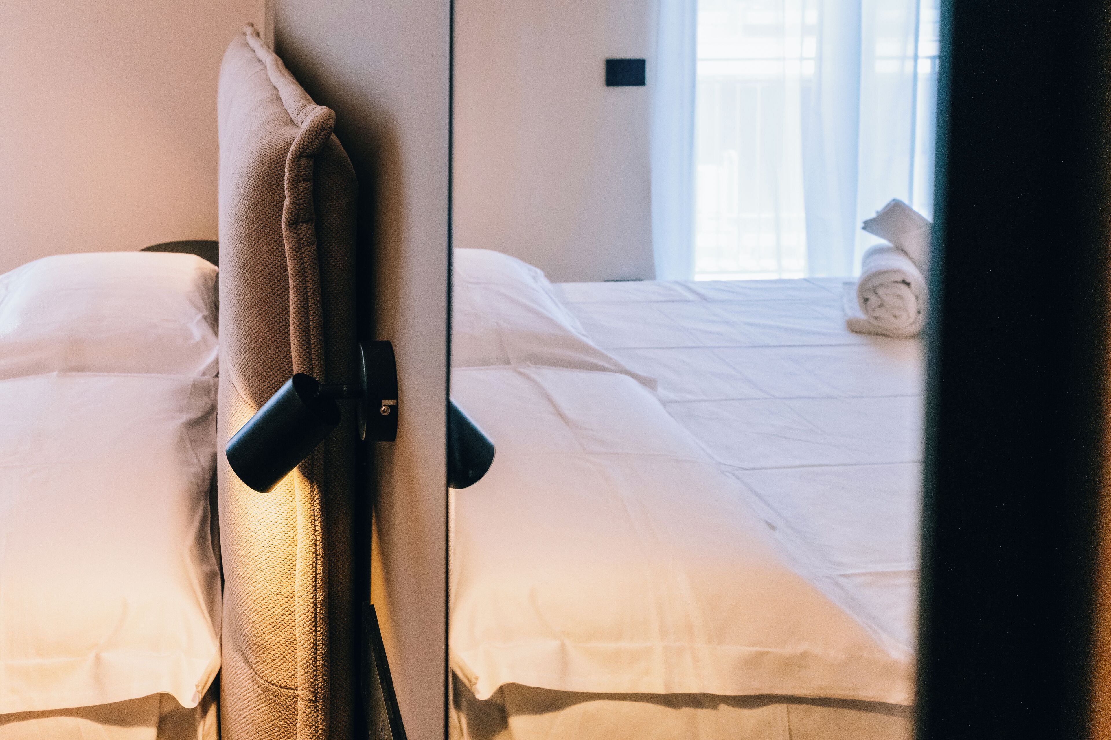 A hotel room with two beds, a window with curtains, and a towel on the bed.