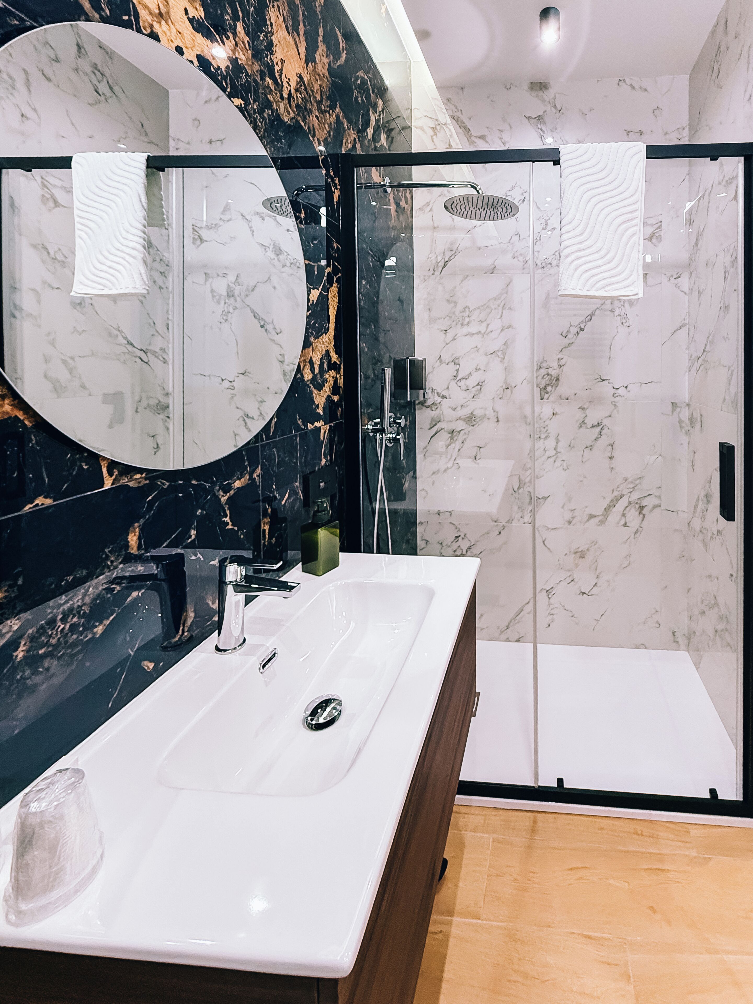 A modern bathroom with a marble vanity, a glass shower enclosure, and a large mirror.