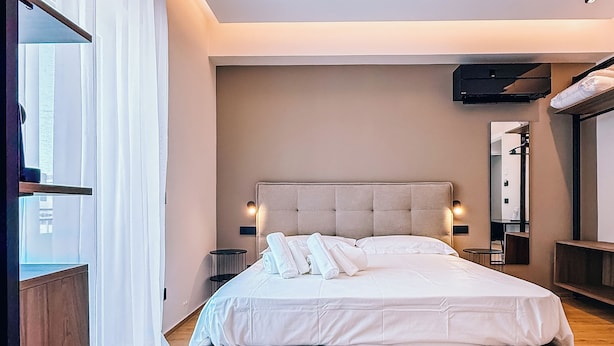 A modern bedroom with a large bed, bedside tables, a mirror, and a wooden floor. - LumiaRooms (Milazzo)