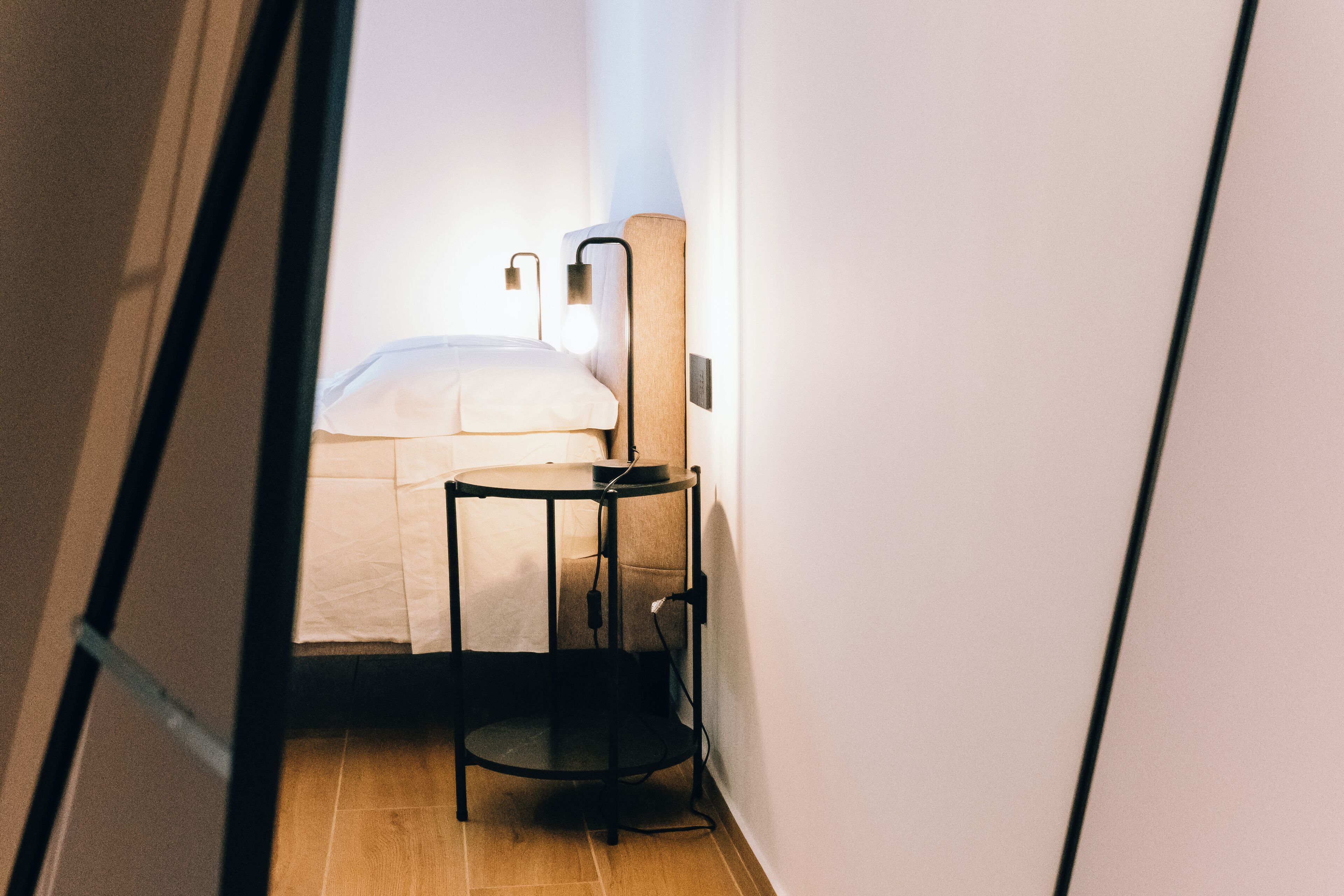 A narrow hallway with a bed and a small table with a lamp.