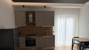 A modern kitchen with built-in appliances, a dining area with a table and chairs, and a large window with sheer curtains. - LumiaRooms (Milazzo)