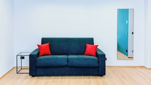 A room with a dark blue sofa, two red cushions, a glass coffee table, and a large mirror on the wall. - LumiaRooms (Milazzo)