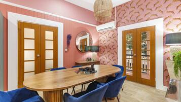 A dining area with a wooden table, blue chairs, a hanging light fixture, and patterned wallpaper.