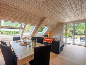 Ein geräumiger Essbereich mit Holztisch und -stühlen, großen Fenstern und Blick ins Grüne.