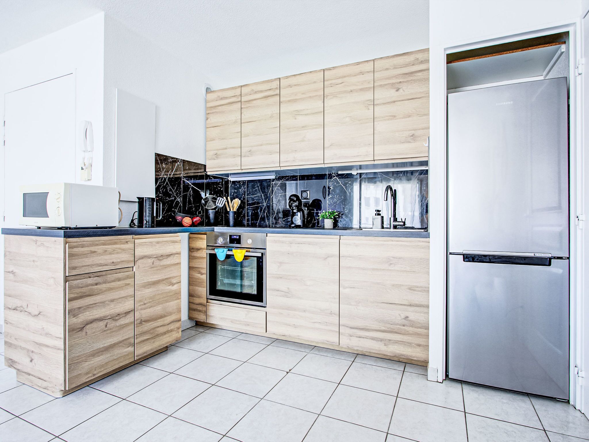 A modern kitchen with wooden cabinets, a built-in oven, a microwave, and a stainless steel refrigerator.