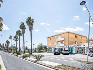 Un immeuble abritant une pharmacie et une boutique médicale au rez-de-chaussée, entouré de palmiers et surplombant un ciel dégagé.