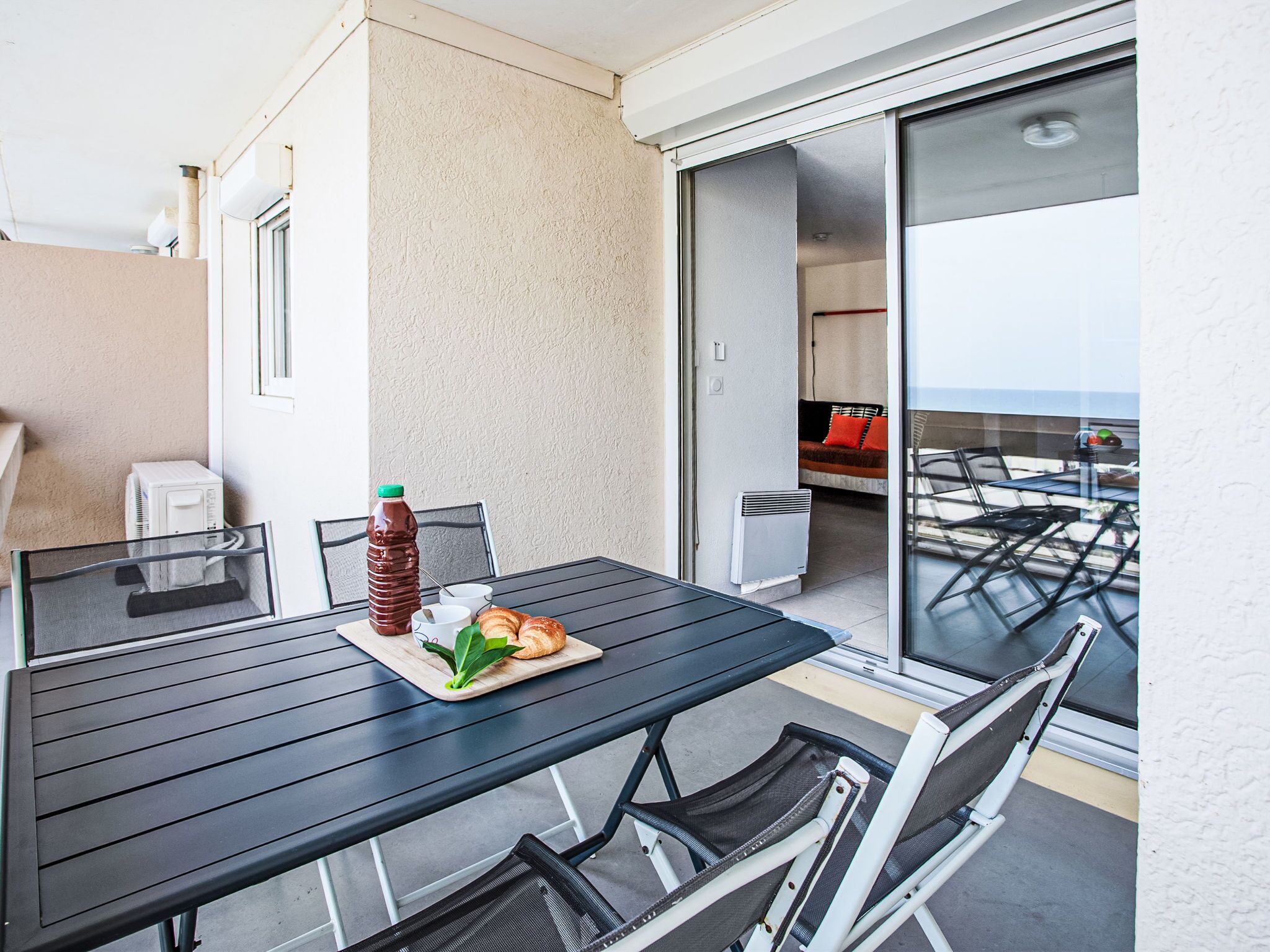 A balcony with a table set for two, a bottle of water, and a plate with croissants.