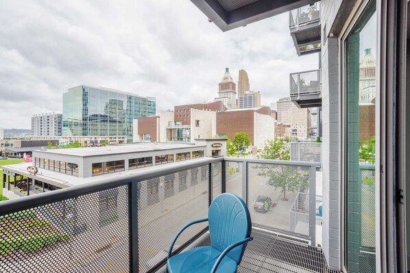 A balcony with a blue chair, overlooking a cityscape with modern buildings and a historic tower.
