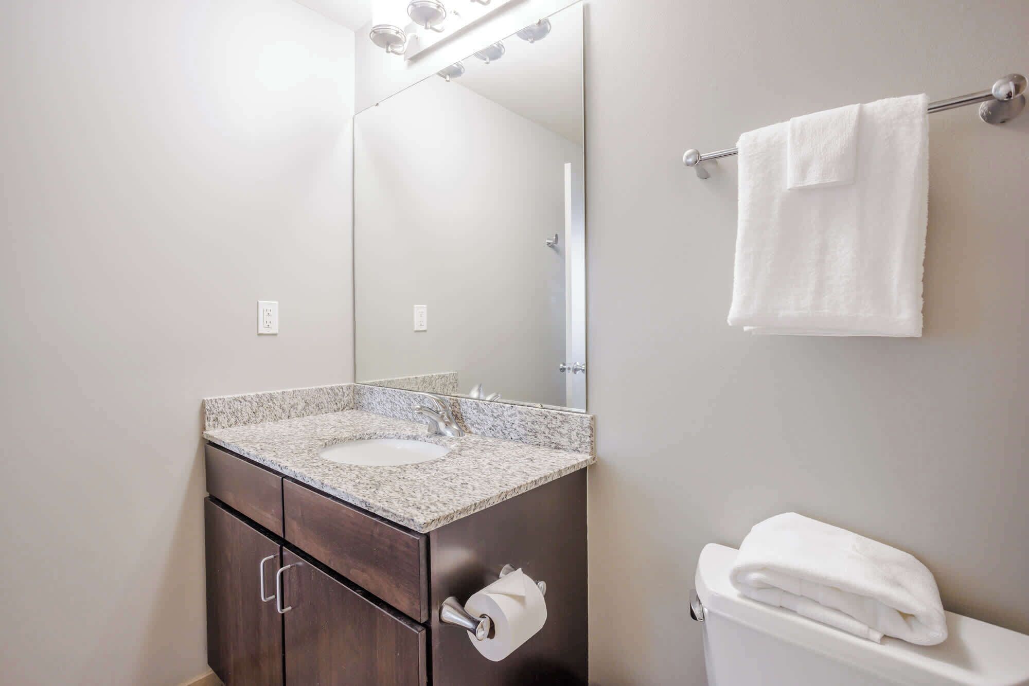 A bathroom with a granite countertop sink, a dark wood cabinet, a toilet, and a towel hanging on a towel rack.