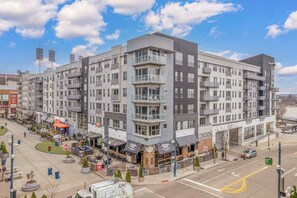 A multi-story hotel with a modern design, featuring balconies, large windows, and a ground-level commercial area with outdoor seating.