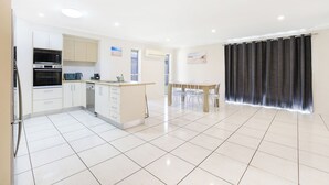 A modern kitchen with white cabinets, a built-in oven, and a coffee maker. There is a dining area with a wooden table and chairs. - Bargara Haven
Welcome to your personal oasis: Coastal calm blends with style. (Bargara)