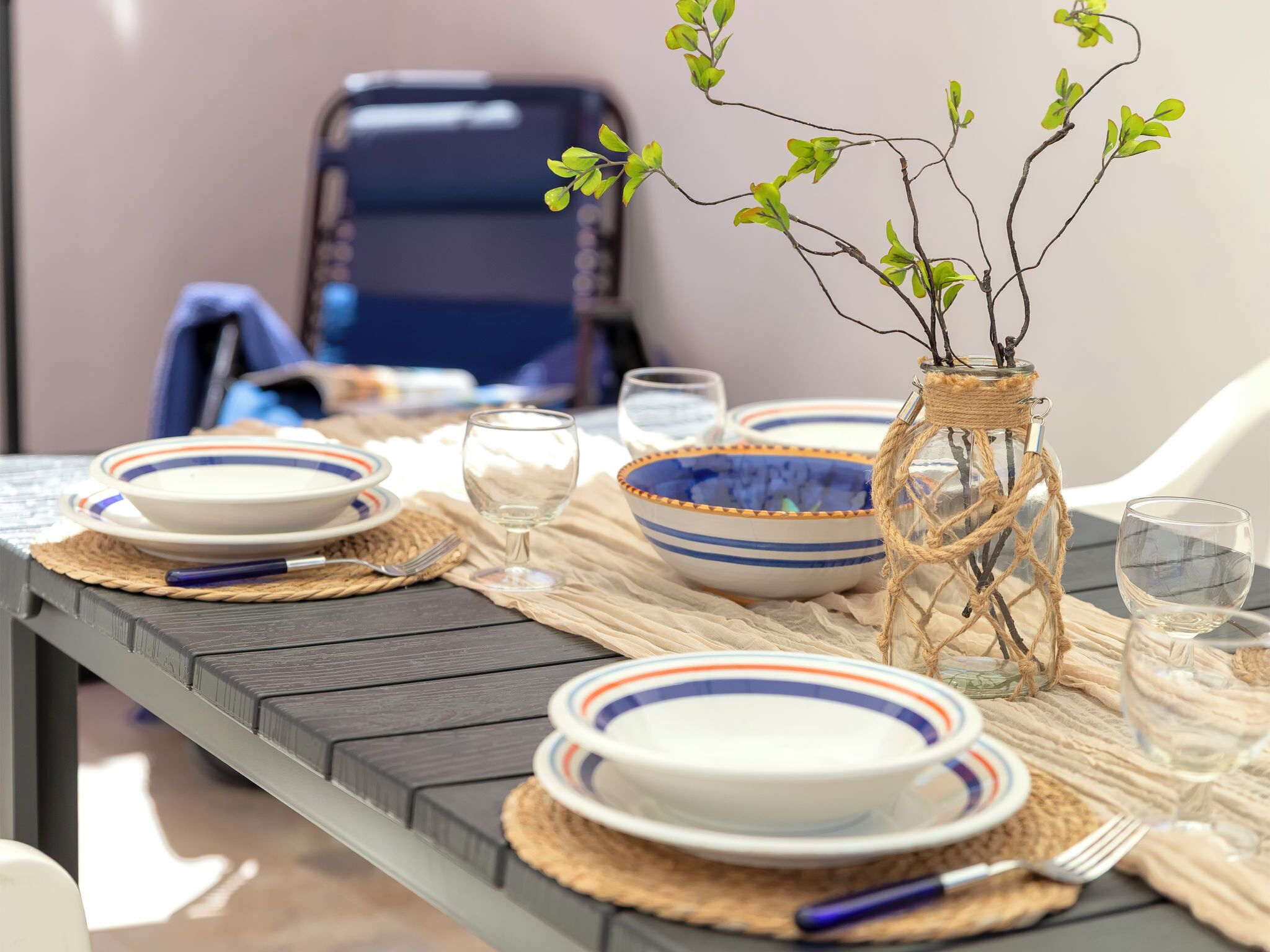 A dining table set with plates, bowls, and a vase with branches.