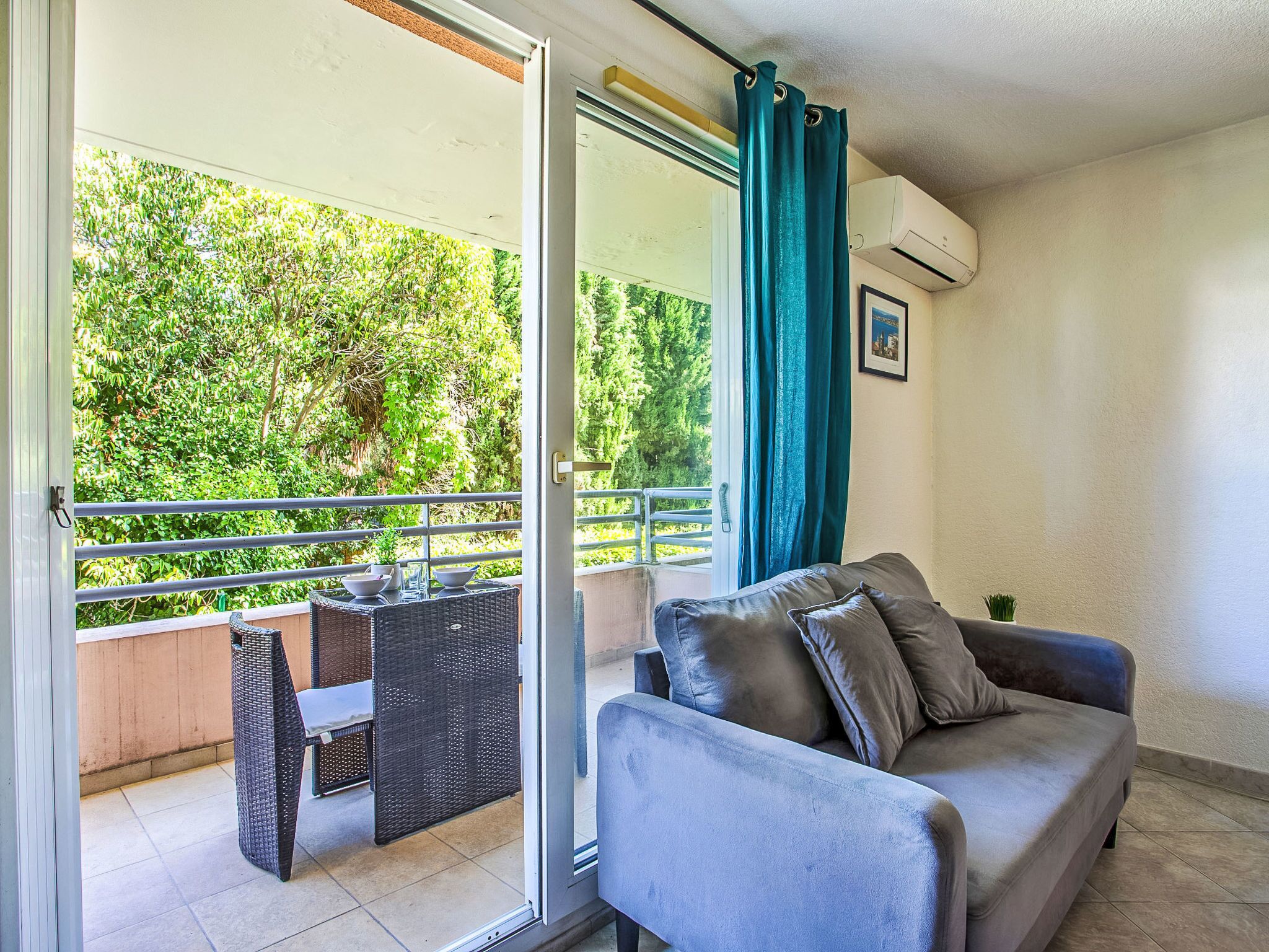 Ein Balkon mit einer Couch und einem Tisch, Blick ins Grüne und ein Fenster mit Vorhängen.