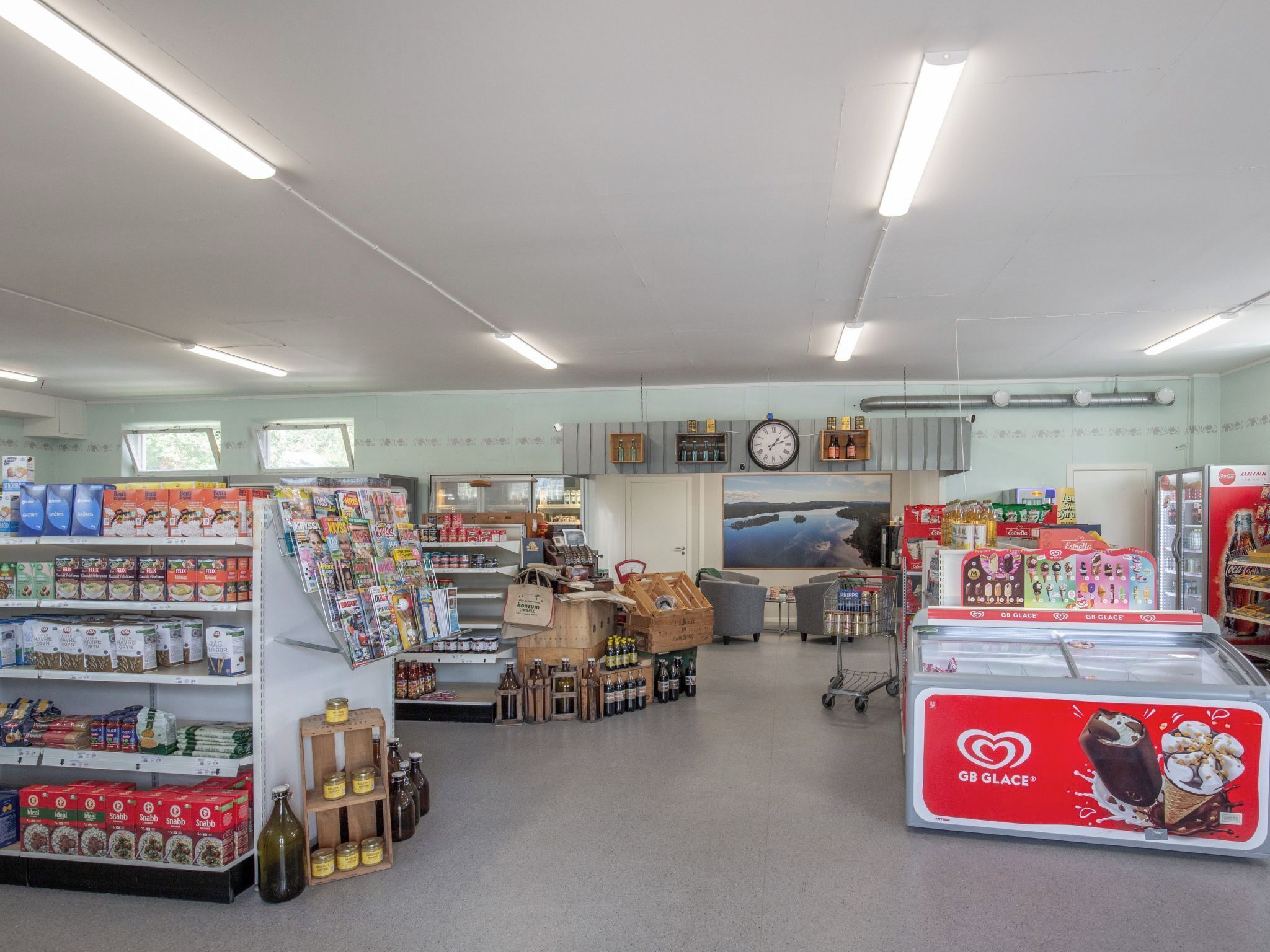 Een supermarkt interieur met schappen vol diverse producten, een vriesvak en een kassa.