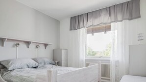 Quarto com cama de madeira, mesa de cabeceira, radiador e janela com cortinas.