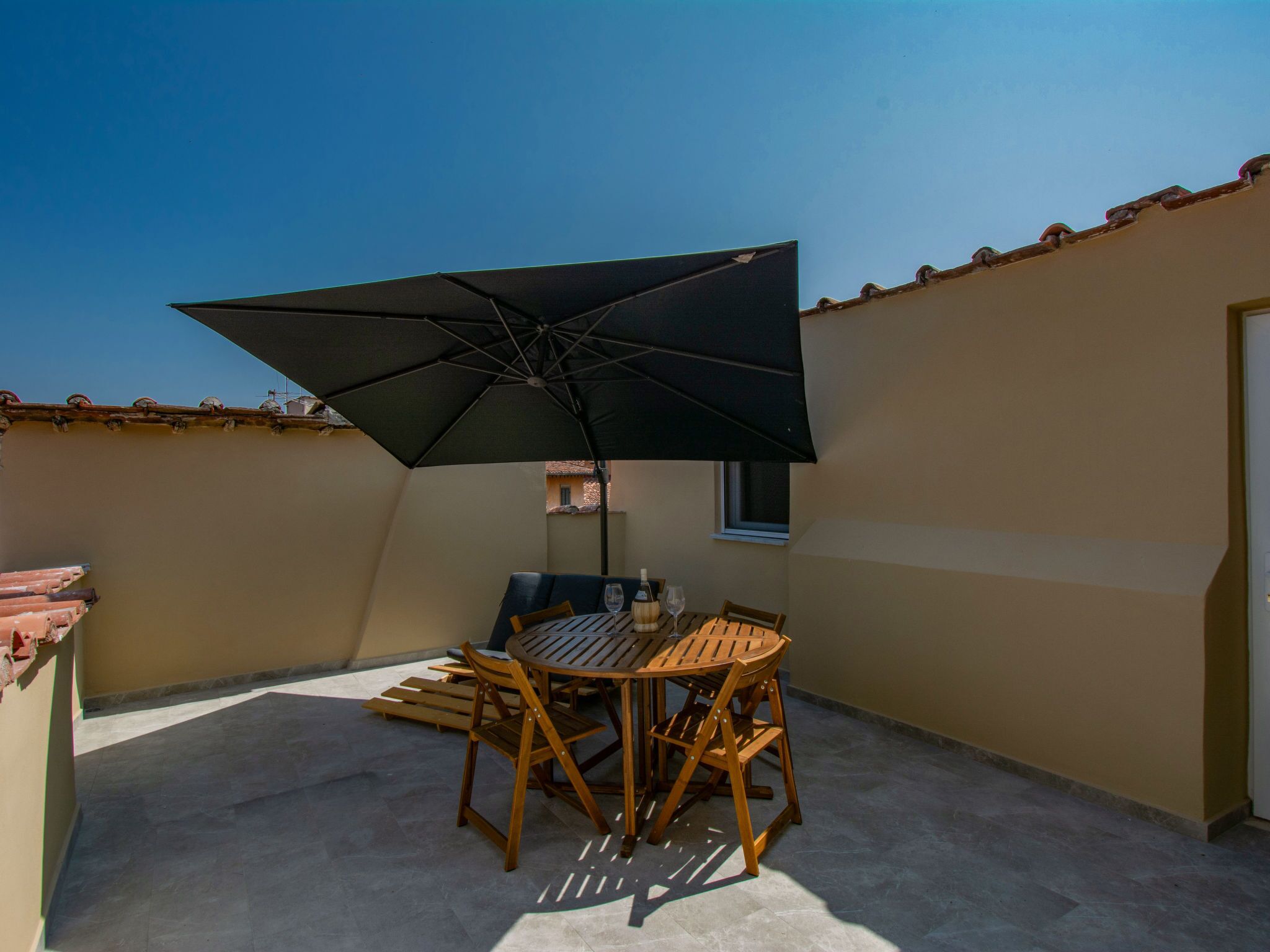 Eine Terrasse im Freien mit Tisch, Stühlen, einem großen Sonnenschirm und einem Fliesenboden.