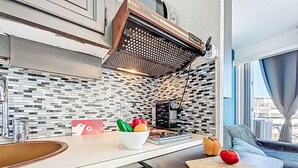 Una cocina moderna con encimera blanca, extractor de humos negro y ventana con cortinas.