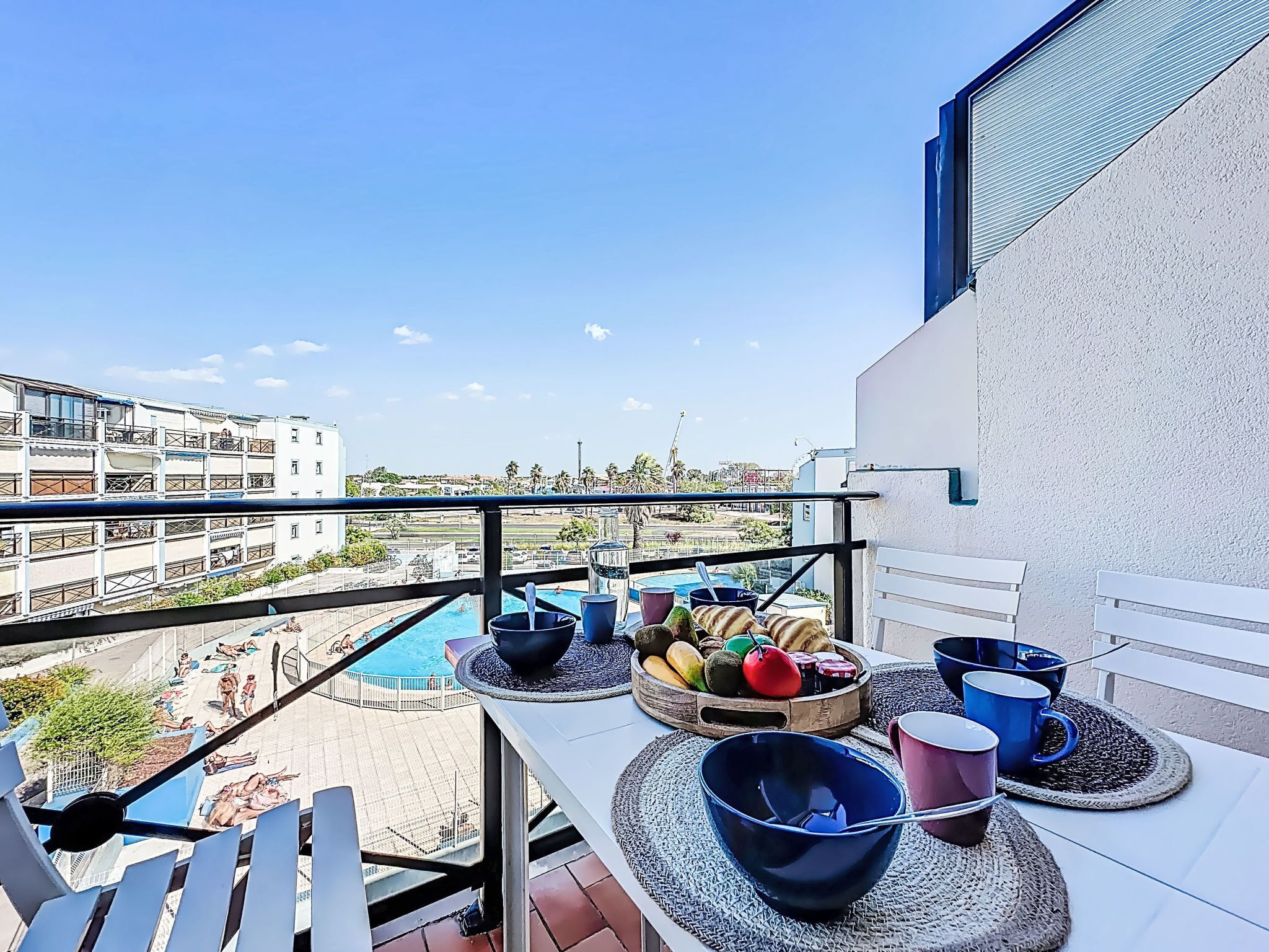 A balcony with a pool view, outdoor seating, and a fruit bowl.