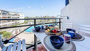 Un balcón con vista a la piscina, mobiliario exterior y un frutero.