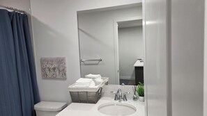 Ein modernes Badezimmer mit einem weißen Waschbecken, einer Toilette und einer Duschvorhang. Ein Handtuchhalter mit gefalteten Handtüchern und ein dekoratives Wandbild über dem Waschbecken.