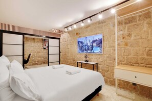 Ein Hotelzimmer mit Bett, Nachttisch, Wand-Fernseher und einer Steinwand.