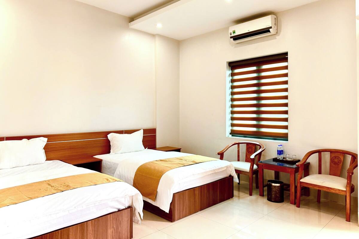 A hotel room with two beds, a desk, a chair, and an air conditioning unit.
