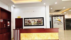 A reception desk with a framed painting above it, a wooden cabinet to the left, and a wall-mounted sign that reads "Sunshine Hotel". - Sunshine Hotel BN (Vo Cuong)