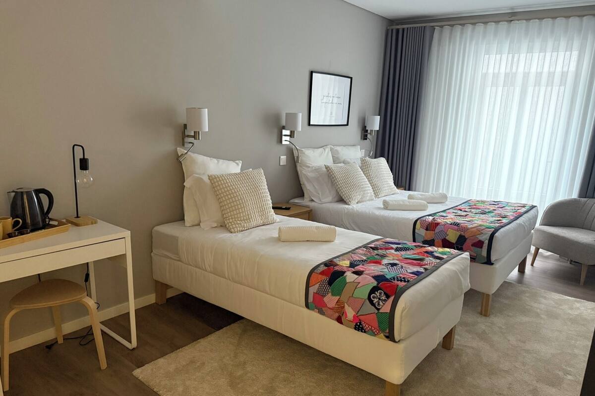 Une chambre d’hôtel avec deux lits, un bureau, une chaise et une machine à café.