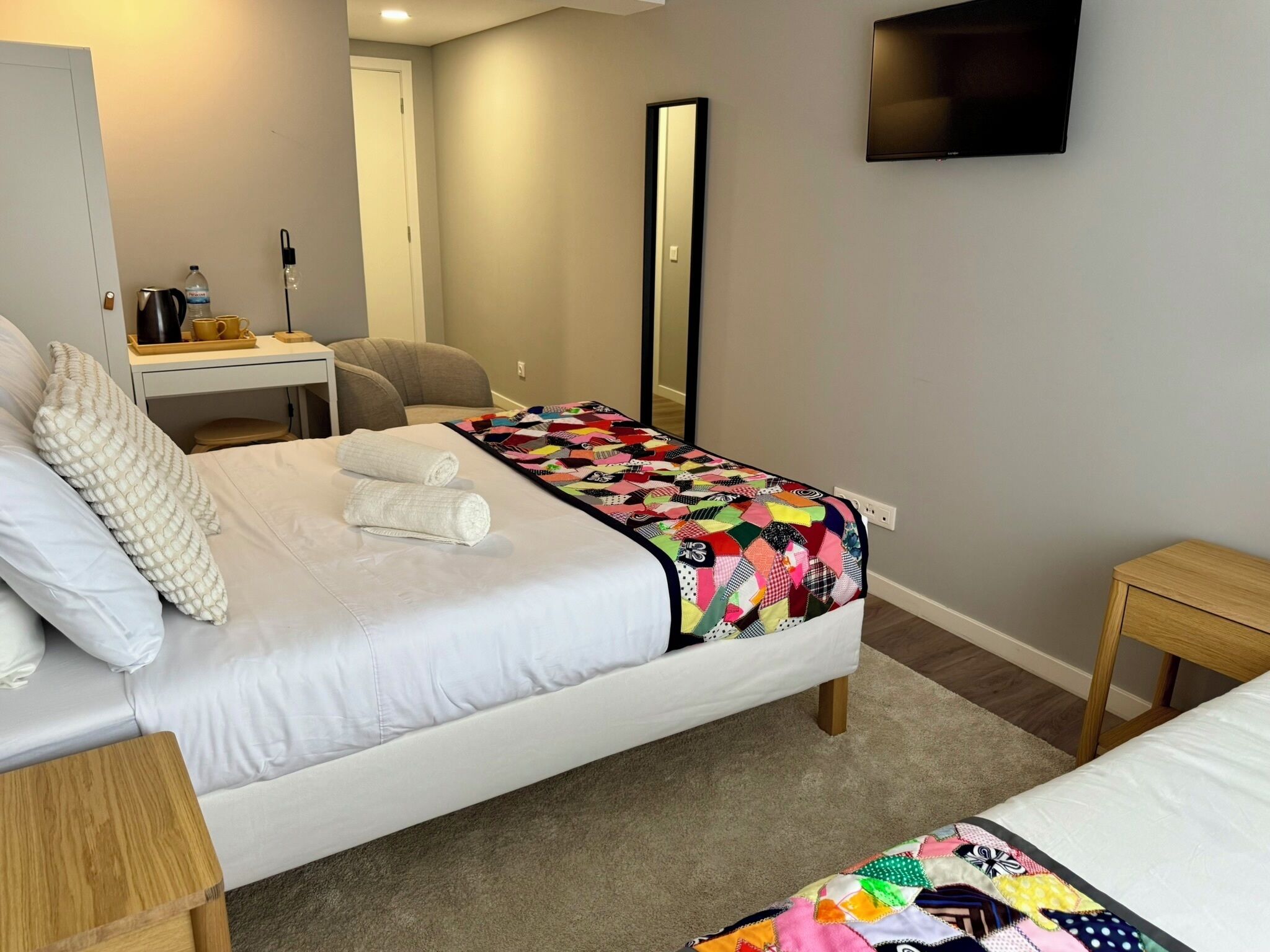 Habitación de hotel con cama, escritorio, silla, televisor y espejo.