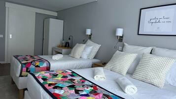 Habitación de hotel con dos camas, colcha colorida, ropa de cama blanca, una cita enmarcada en la pared y una mesita de noche pequeña con lámpara.