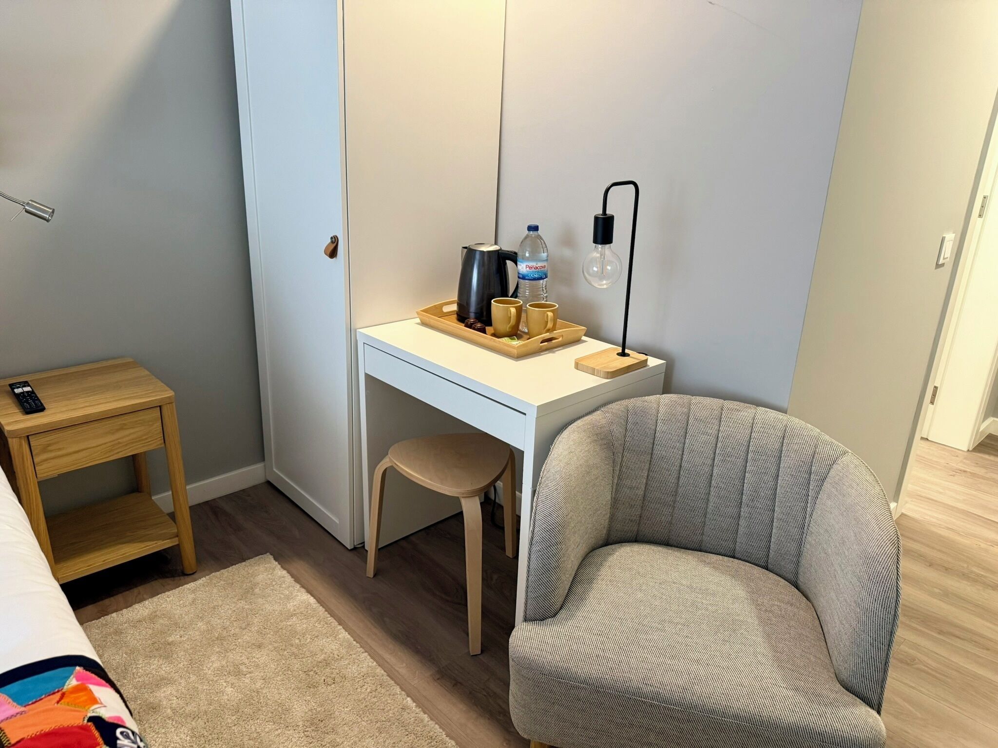 A small, neatly organized room with a white desk, a chair, a small wooden side table, and a rug.