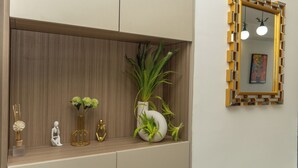Un estante de madera con adornos, incluyendo un jarrón blanco con plantas verdes, un jarrón dorado y una escultura blanca.