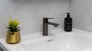 A bathroom sink with a modern faucet, a bottle of hand wash soap, and a decorative plant in a gold vase. - BLOSSOM (Nairobi)
