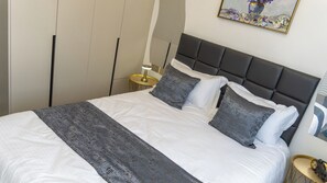 A neatly made bed with a grey and white bedspread, two grey pillows, and a grey headboard. - BLOSSOM (Nairobi)