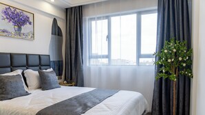Una habitación de hotel moderna con una cama grande, una planta en maceta y vistas a la ciudad a través de la ventana.