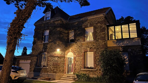 A stone house with a well-lit entrance and a garage. - 1 studio apartment for rent in Villa Amenaide: 1 bedroom, plus kitchen, dining room, and living room (Roisel)