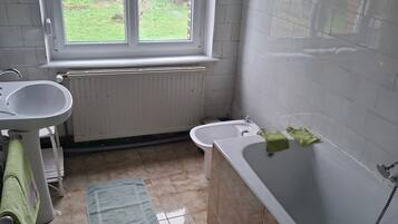 Een badkamer met een raam, twee wastafels, een badkuip en een radiator.